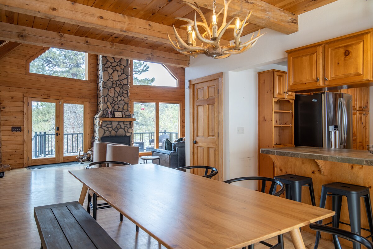Dining area with an antler chandelier, kitchen bar, and stone fireplace view at Wildcat Cabin